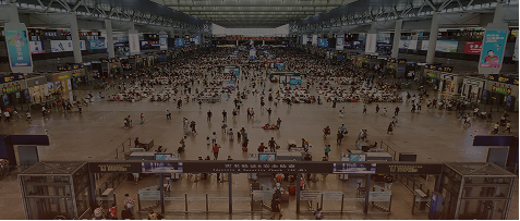 High-angle view of a crowded modern transit terminal concourse with passengers waiting and walking through ticket gates.
